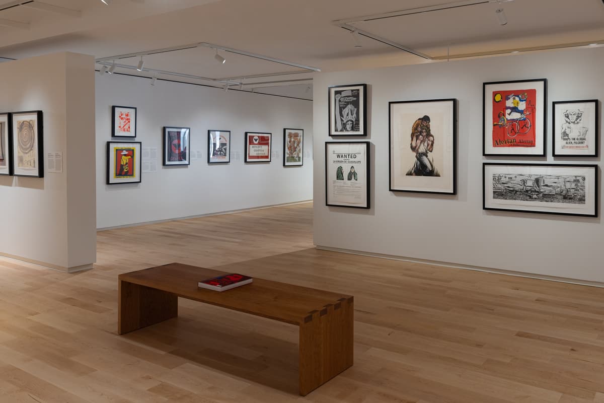 Gallery view with a wooden bench and framed posters and prints depicting protest themes, labor rights, and resistance figures