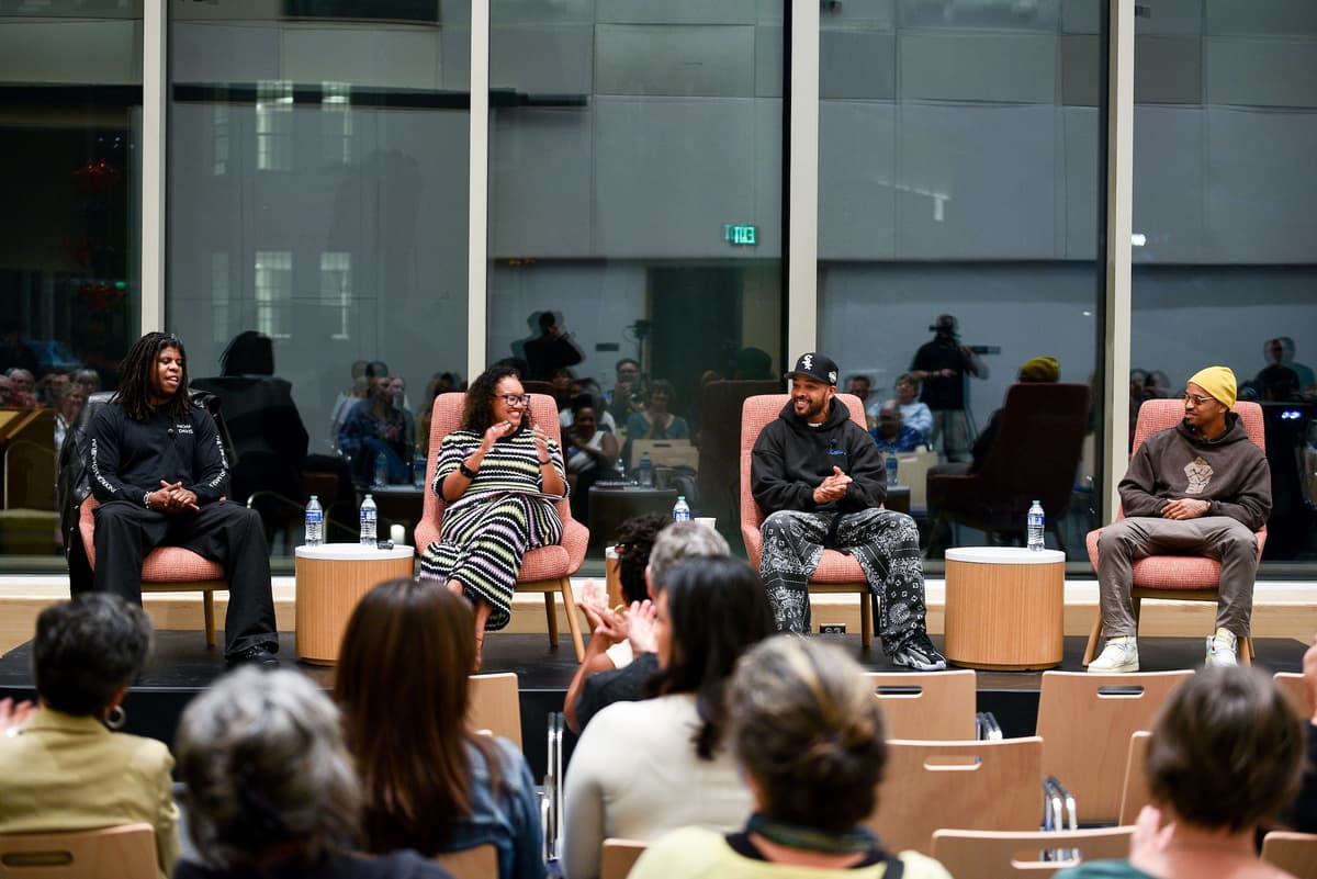 Four individuals seated on a stage in conversation and clapping.