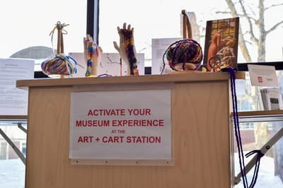 Display setup at an Art + Cart Station with mannequin hands, colorful yarn, and an instructional sign.