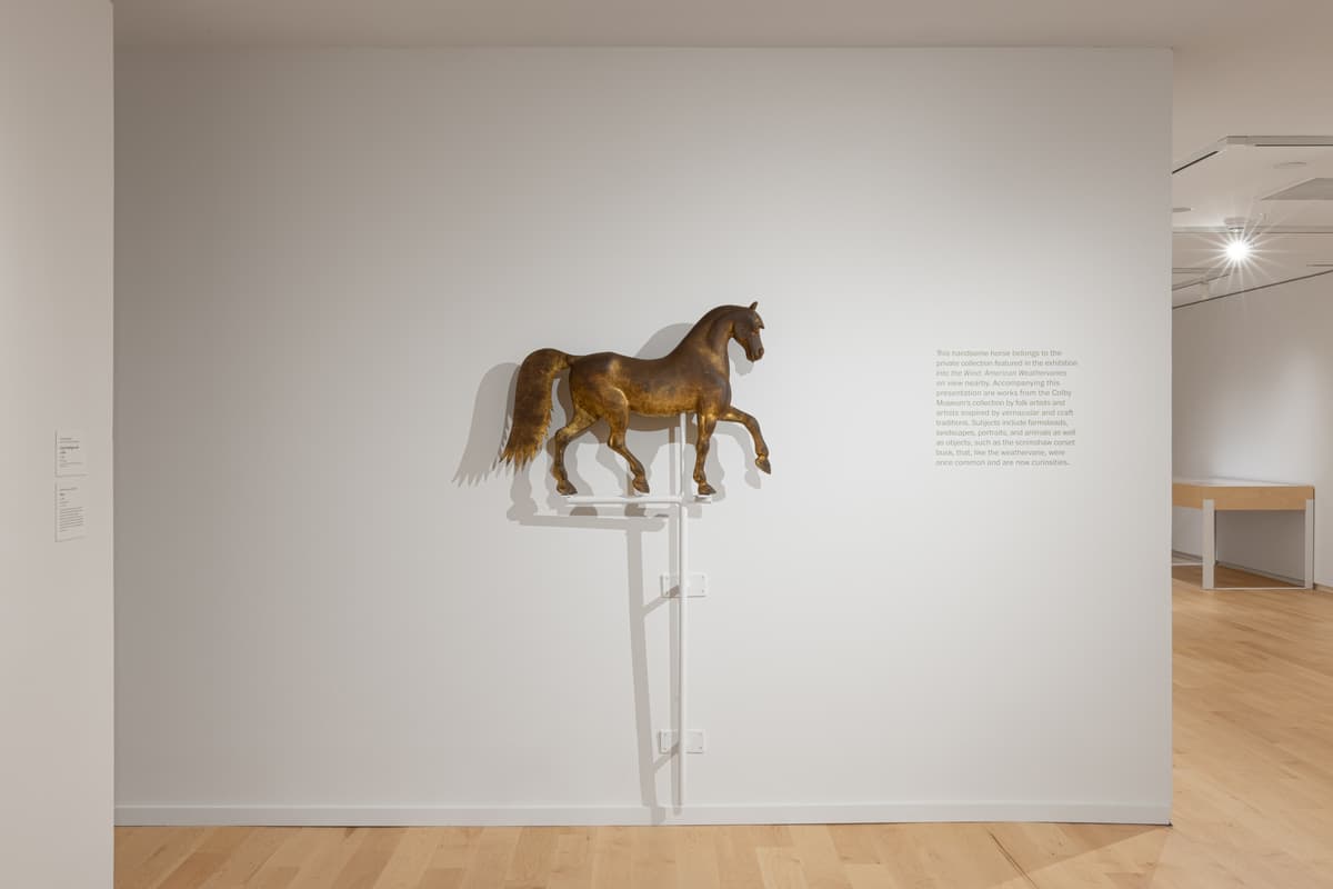 Wall-mounted gilded horse weathervane with accompanying wall text.