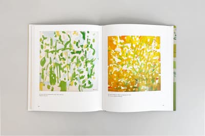 Photograph of the interior of a book with two artworks, one on each page. The left page shows a painting of green and white flowers, and the left page shows orange and green flowers.