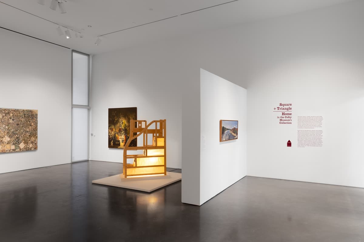 A central illuminated sculpture, paintings on surrounding walls, and wall text "Square + Triangle"