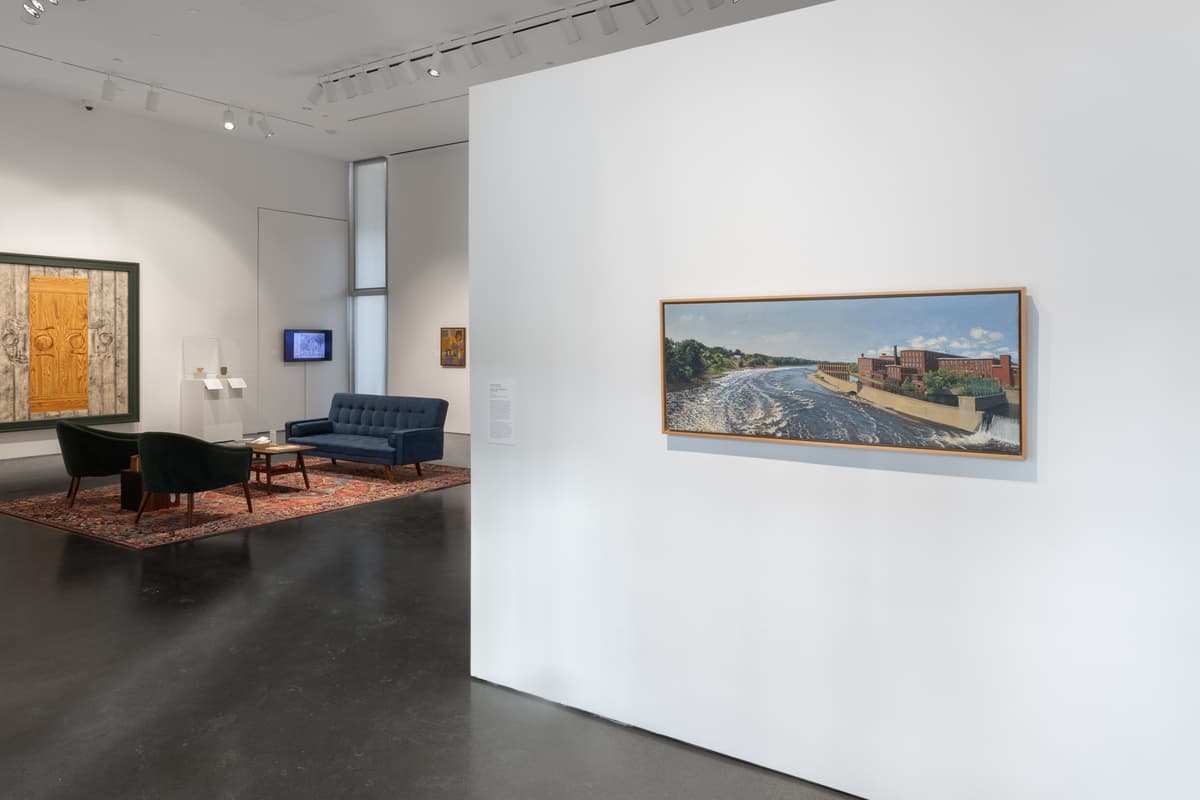 A panoramic painting of a river scene on a white wall; lounge seating and framed art viewable in the background
