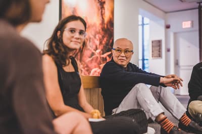 2019 visiting artist Phong Bui seated in a gallery with students