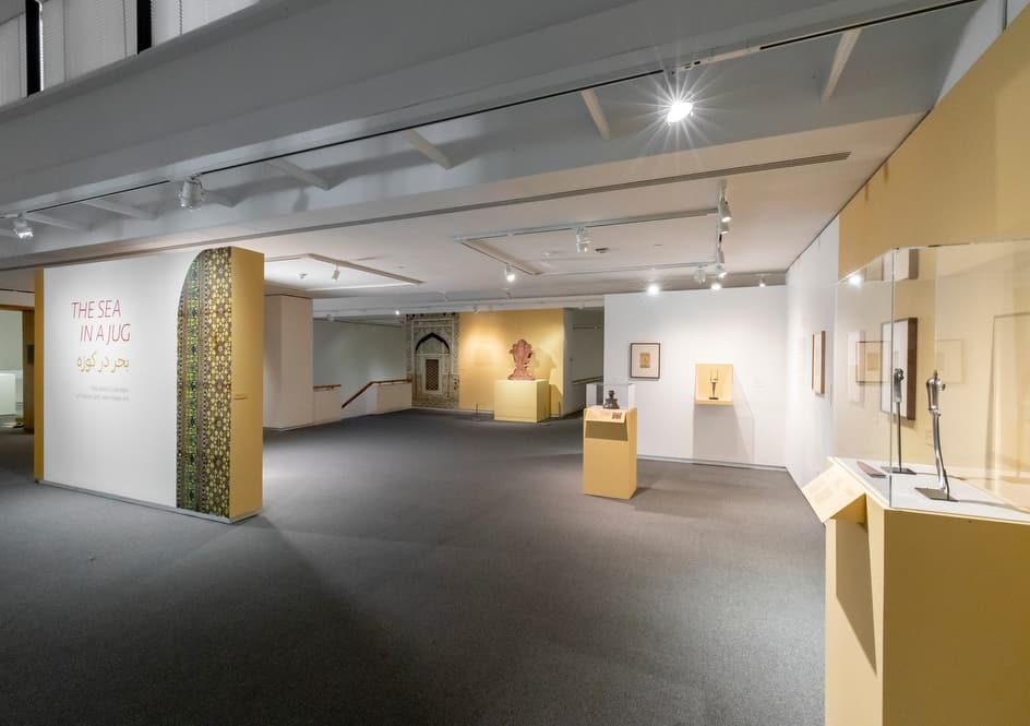 Wide view of exhibition entry, flanked by display cases and wall-mounted artworks across the gallery