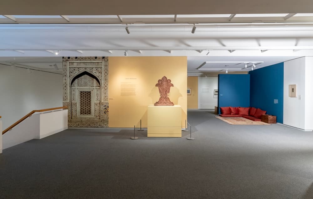 Gallery featuring an ornate architectural arch, central sculpture on a yellow pedestal, and a seating area with red cushions in the background