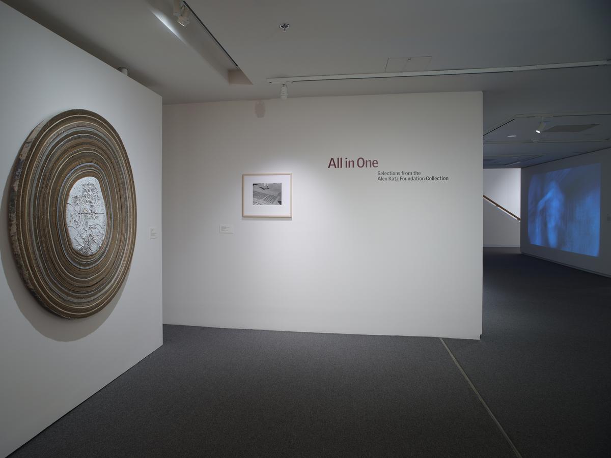 A large wall mounted circular sculpture and a framed work next to vinyl lettering on the wall with the exhibition title.