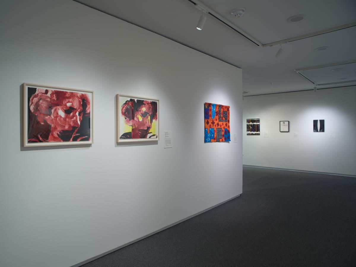 Three works hung in a row including two portraits depicted in red; a second wall visible in the background with additional three works in a row are visible.