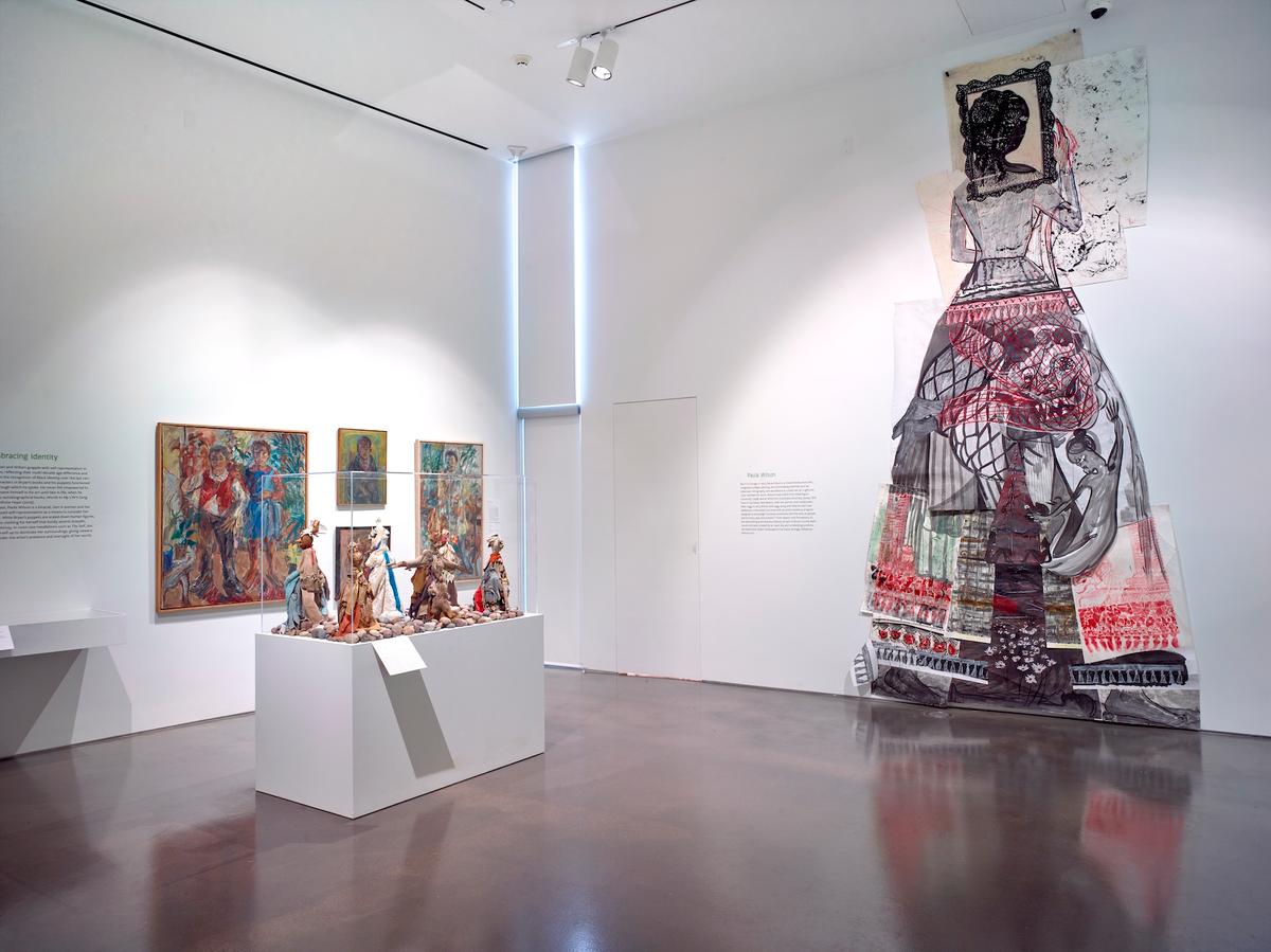 Large mixed-media installation anchored on the wall, flanked by colorful paintings and figurative sculptures.