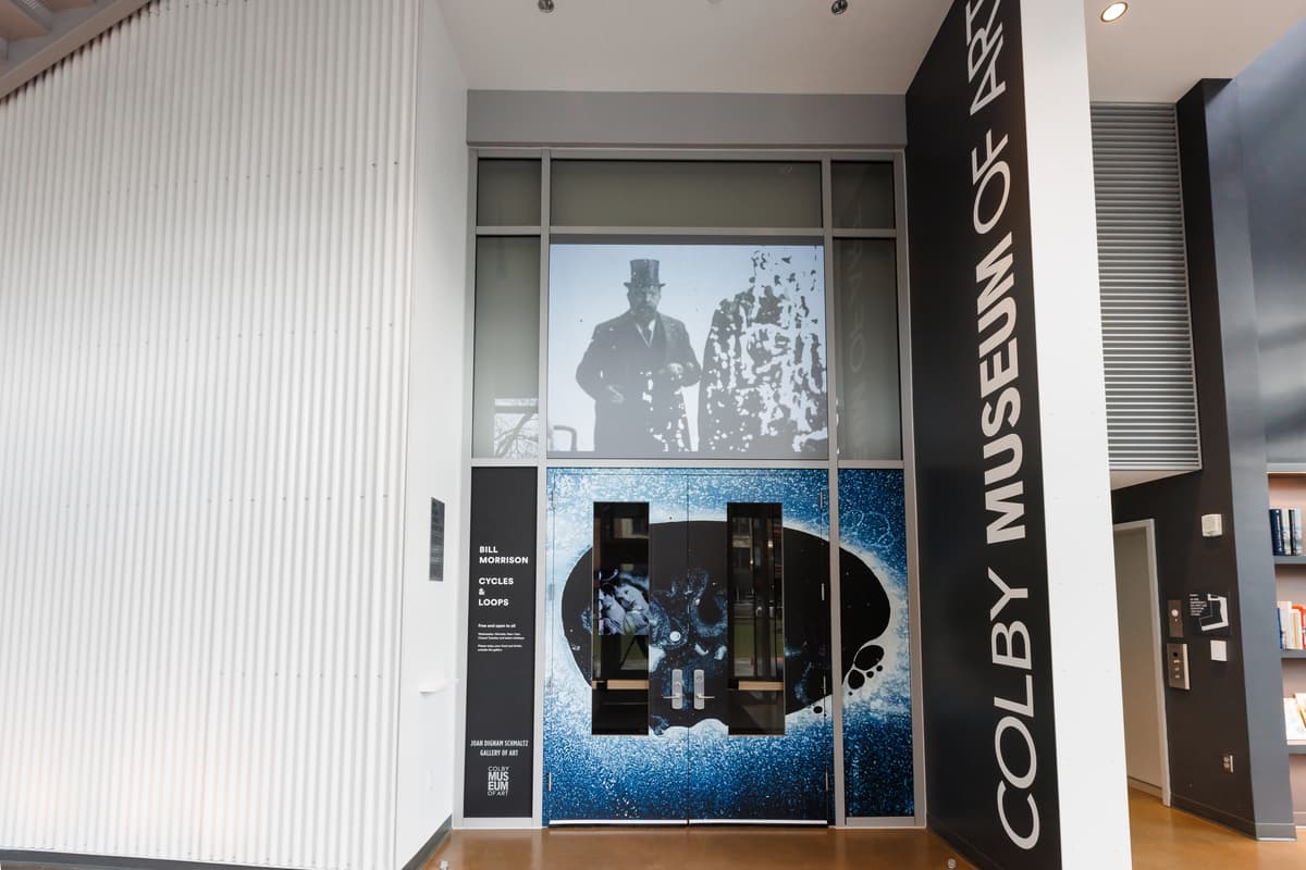 Entrance to the gallery with a projection of a man in top hat and overcoat above double doors.