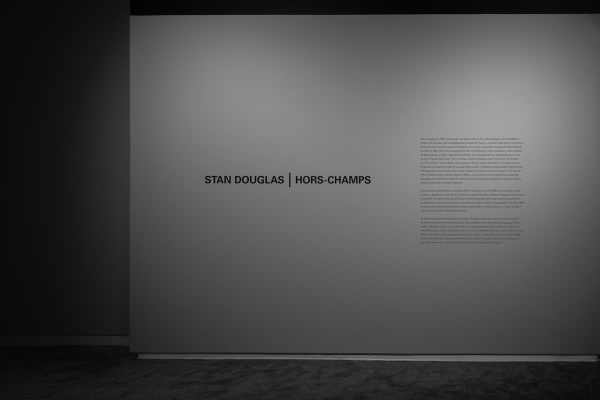 Gallery wall with the text “STAN DOUGLAS | HORS-CHAMPS” and an exhibition description label to the right