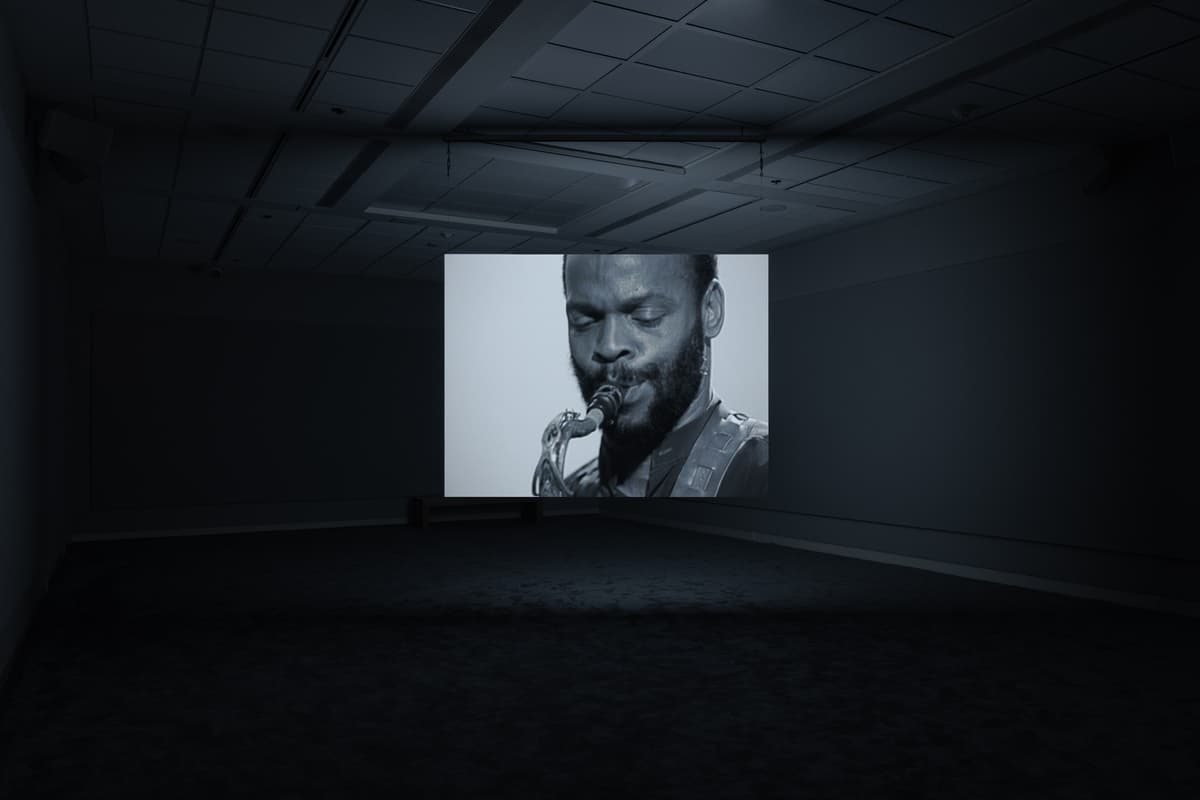 Dark gallery space with a projected black-and-white image of a man playing a saxophone