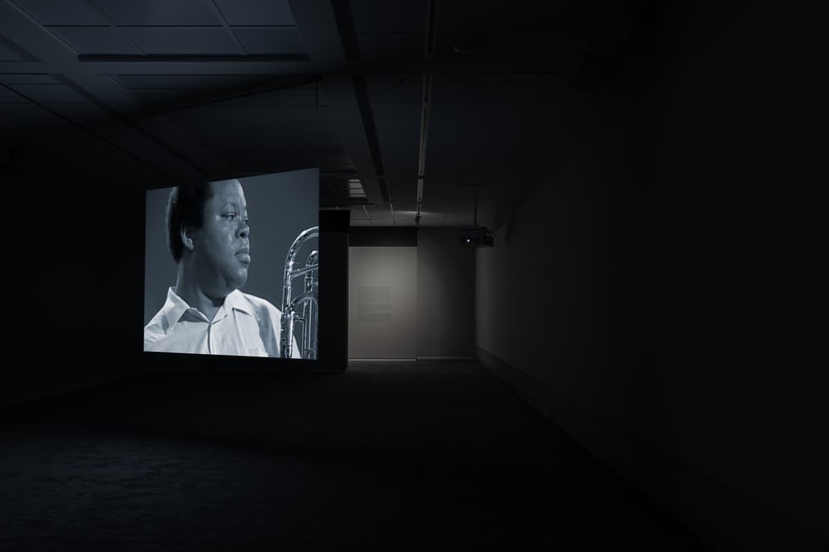 Dark gallery space with a large projected black-and-white image of a man playing a brass instrument