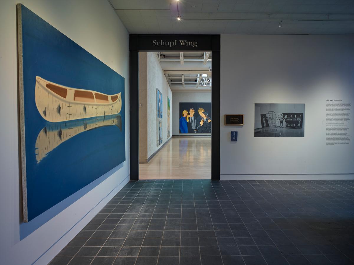 Doorway to Schupf Wing gallery with a large painting of a canoe and its reflection in still water to the left. Figurative paintings are visible through the doorway.