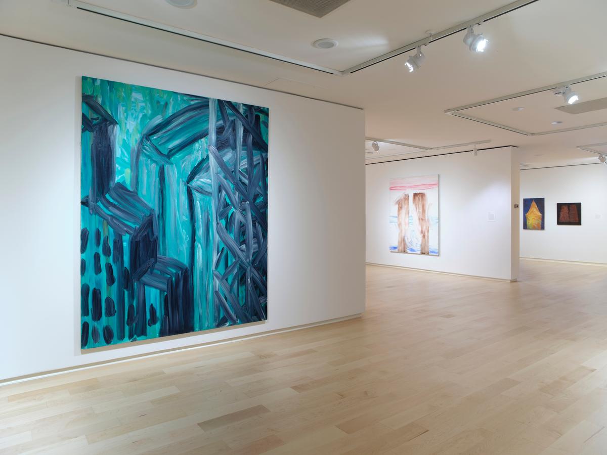 Large abstract painting in shades of teal and black on a white wall, with additional colorful works visible in the background.