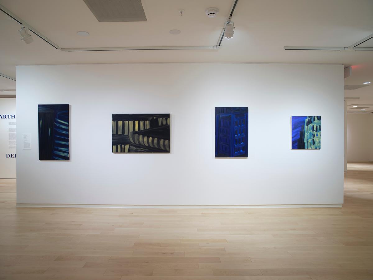 Four abstract paintings in varying shades of blue and black are displayed in a row on a white wall.
