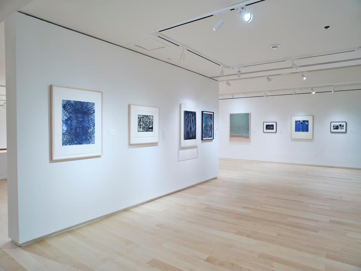 Gallery with white walls and light wood floors displaying colorful and monochrome abstract prints