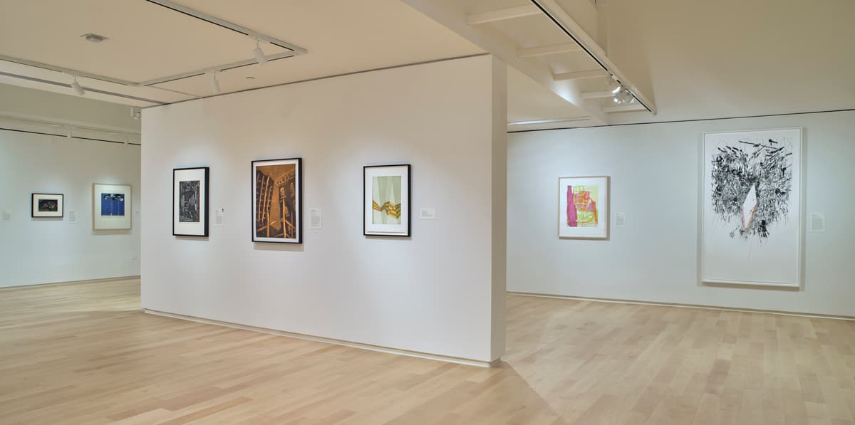 Framed abstract and figurative works on white walls in a light-wood gallery space