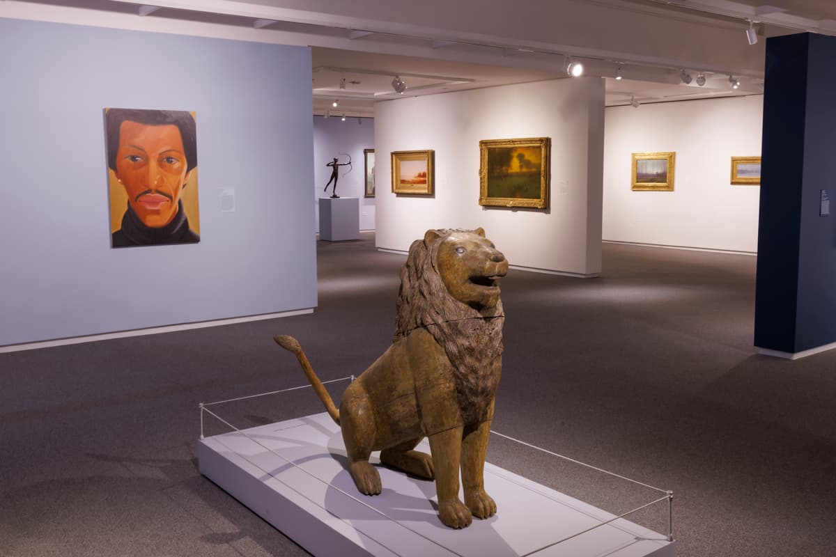 Wooden lion sculpture on a low platform with a portrait on the left wall and landscape paintings in the background