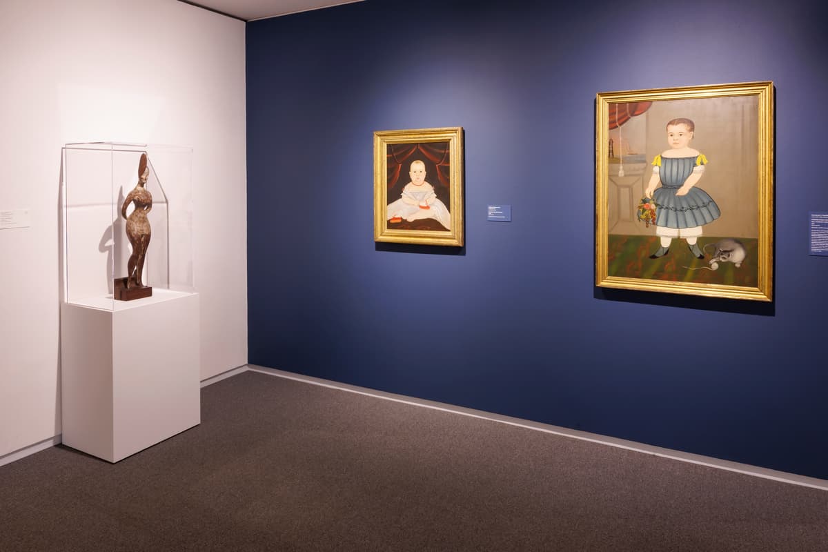A bronze sculpture in a vitrine and two portrait paintings on a dark blue wall