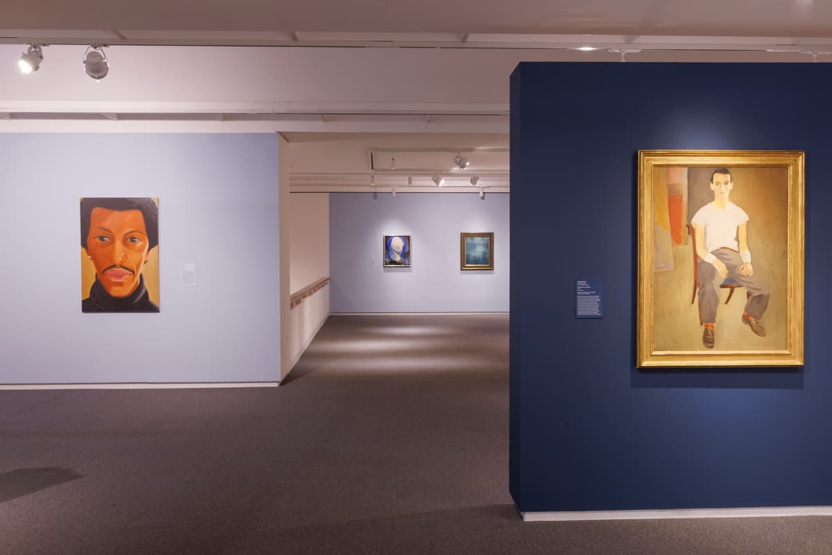 Two portrait paintings, each on a blue wall; additional framed works visible in the distance.