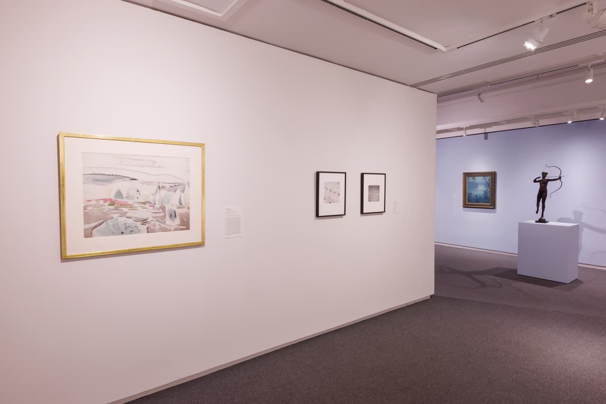 Three framed works on a white partition wall and a bronze figurative sculpture visible in the background.