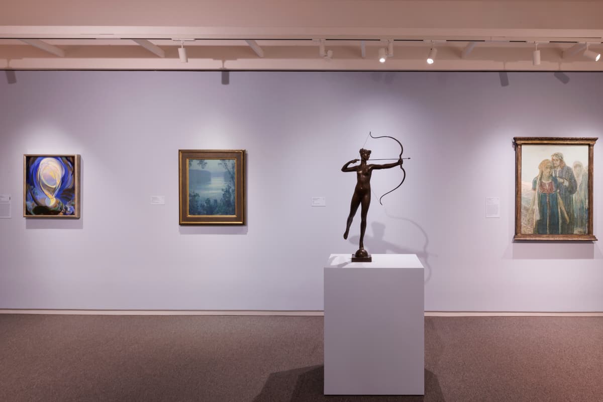 A bronze sculpture of an archer and three framed paintings on a lavender wall.