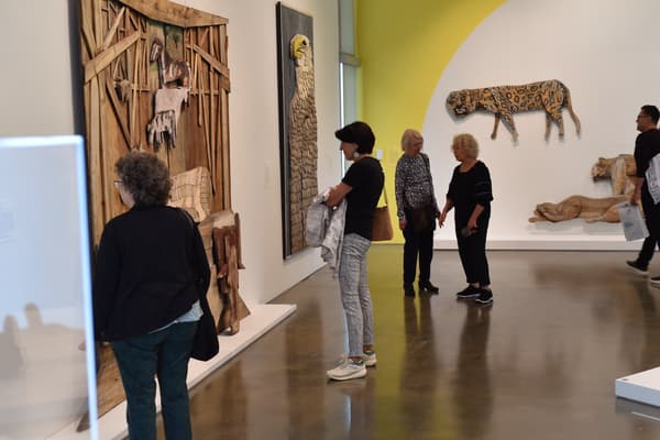 A group of people look at a large wood sculpture installed on a wall