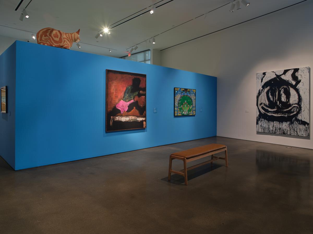Three paintings installed in a gallery, two on vivid blue wall with cat sculpture perched on top.