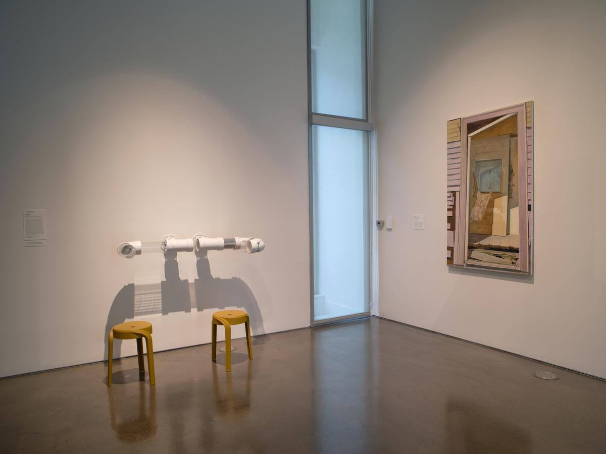 Corner with two yellow stools and a nearby framed painting on the wall.