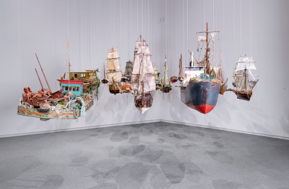 Installation of suspended model ships clustered together in a white gallery corner
