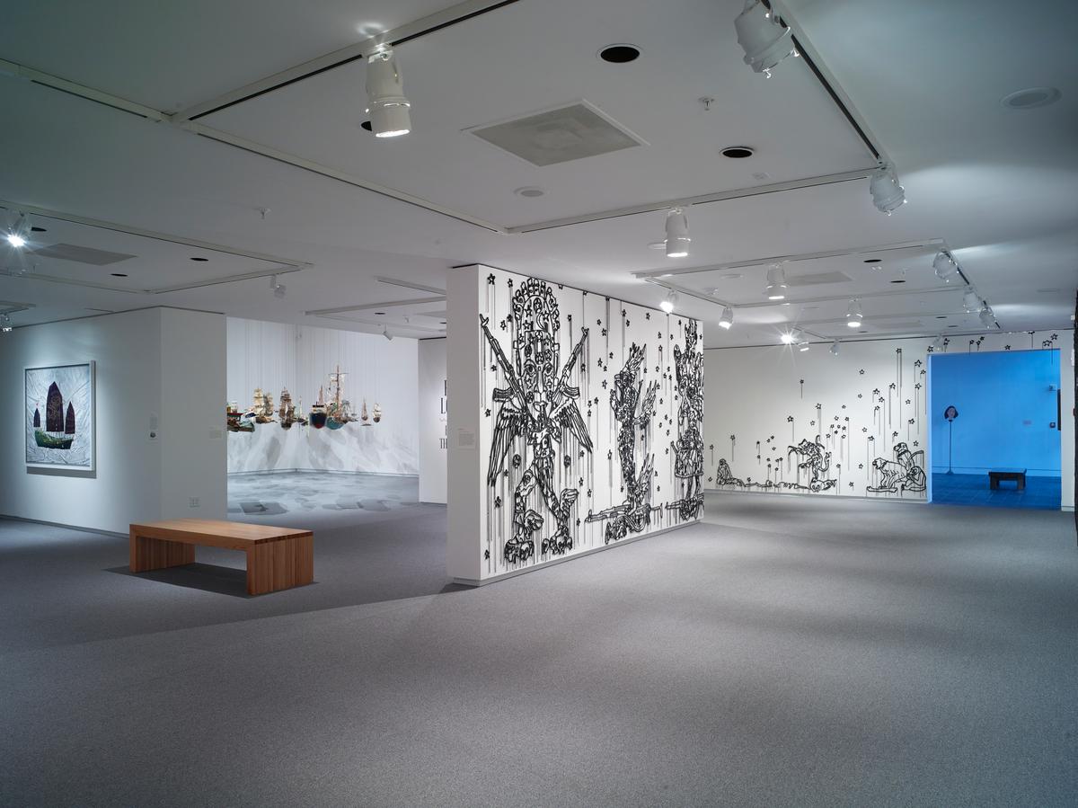 Wide gallery shot with beaded wall illustrations, suspended boats, and benches arranged throughout the space