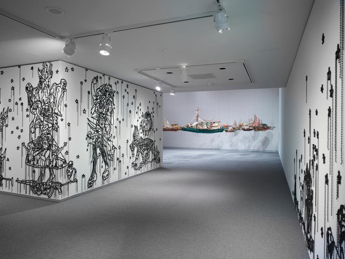 Corridor view with beaded wall illustrations on the left and suspended boats installation visible in the distance