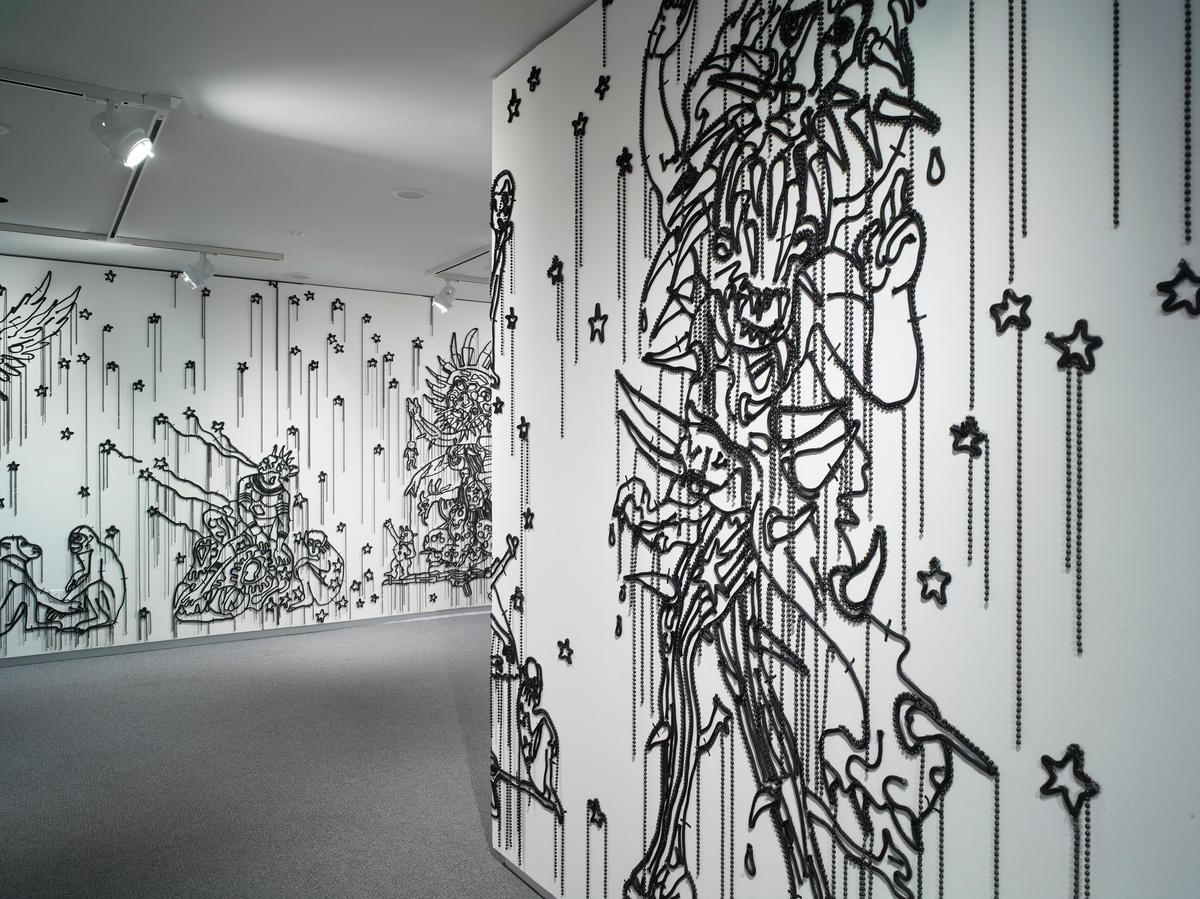 Black beaded wall installation depicting abstract figures and stars on a white gallery wall