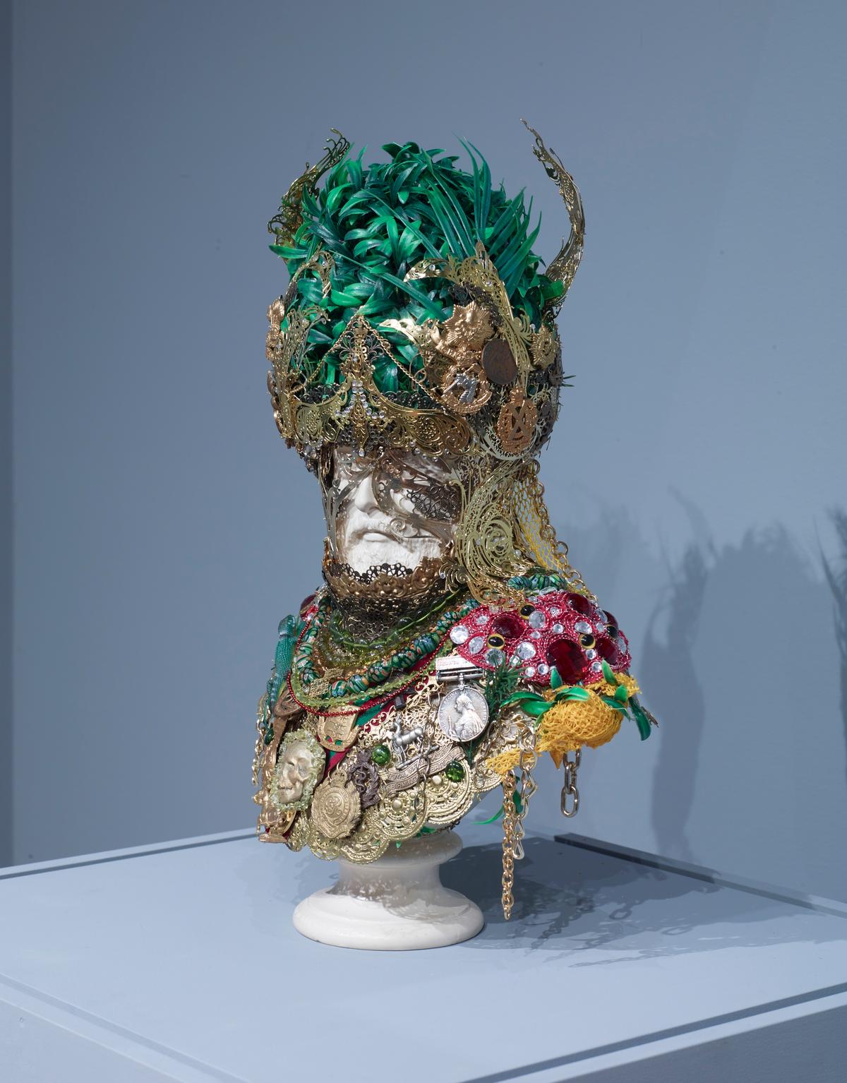 White bust sculpture adorned with gold ornaments, set against a bluish-gray background