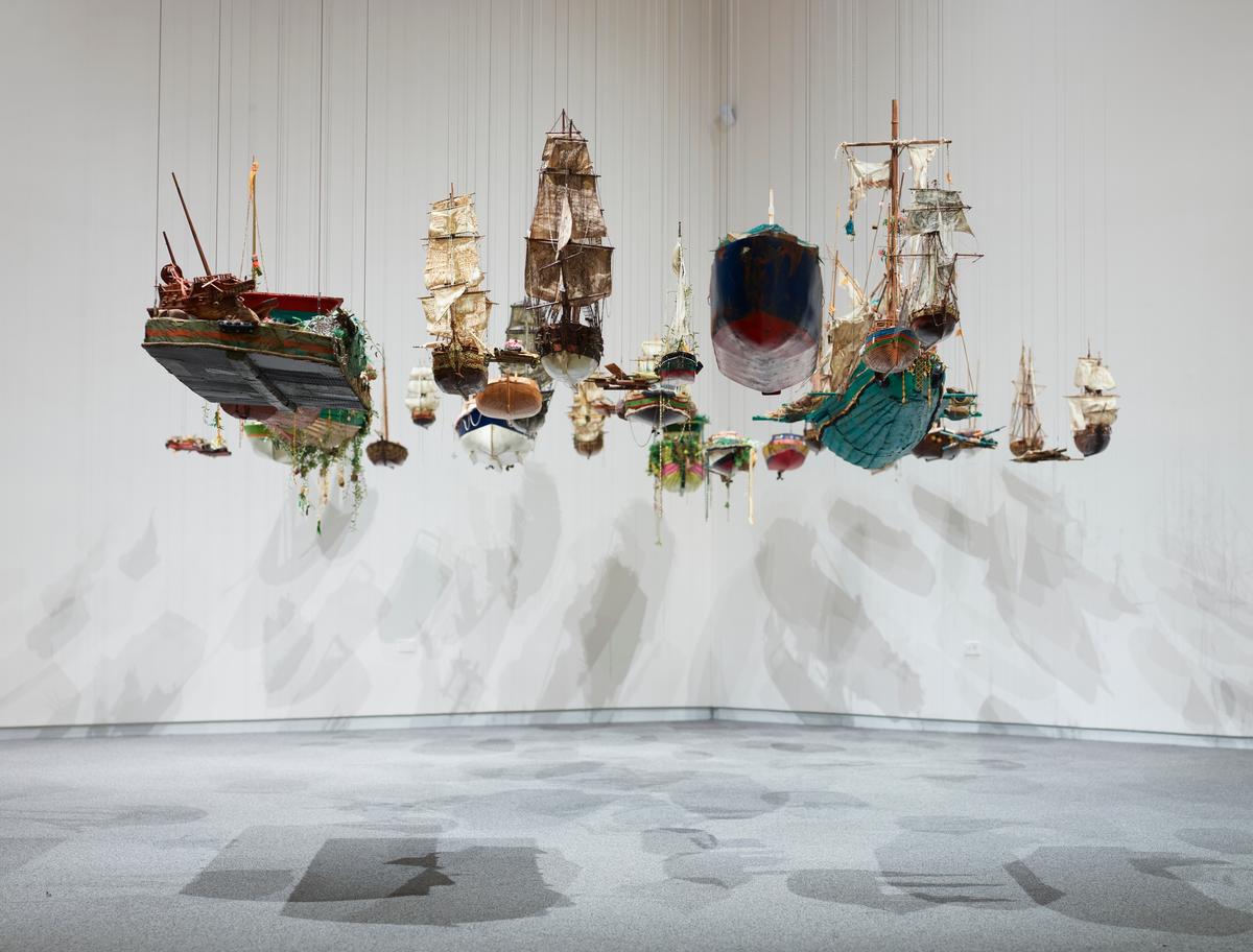 Dozens of model ships suspended from the ceiling, casting shadows on white walls and gray floor