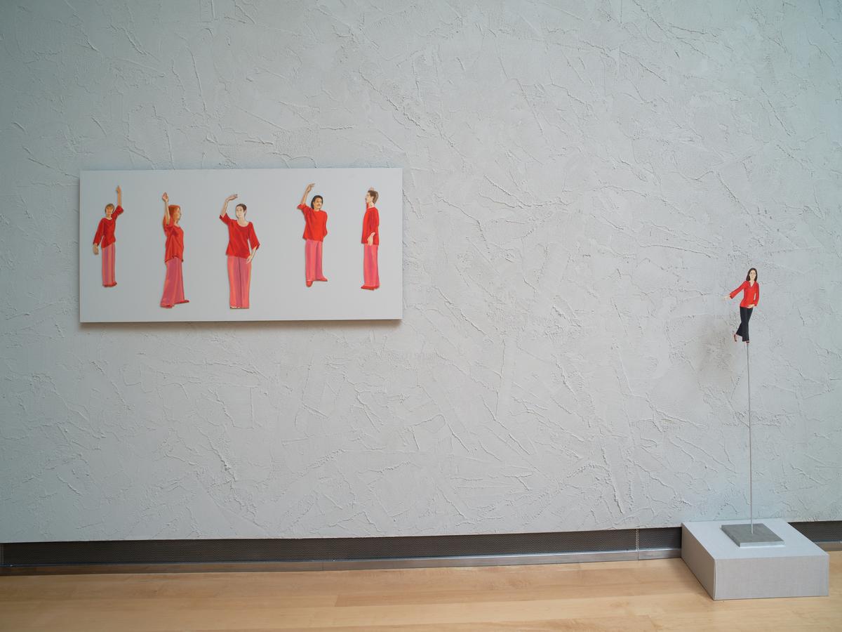 Painting of five figures in red clothing performing gestures beside one a small matching sculpture of a woman in red posed on a plinth to the right.
