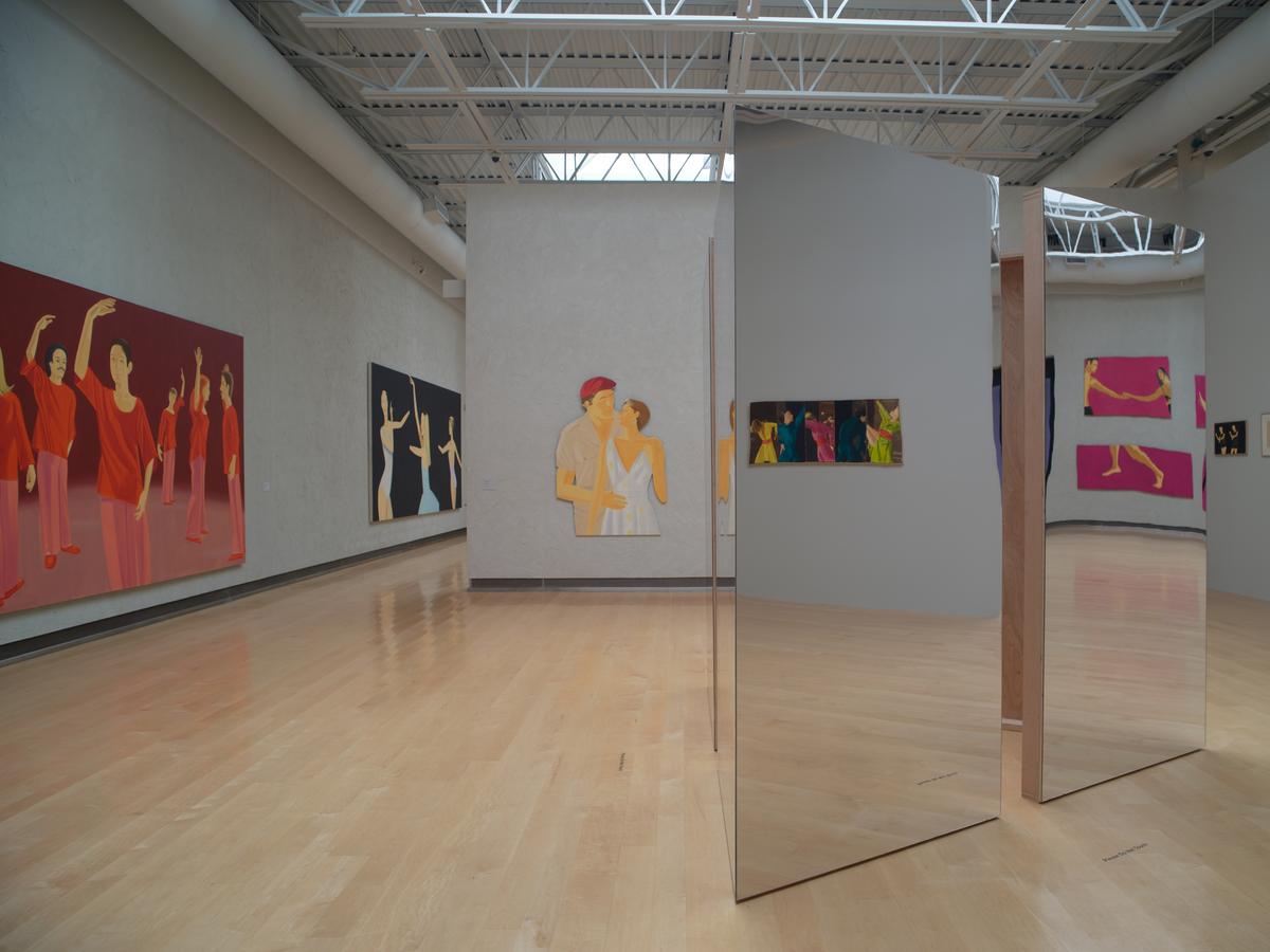 Sculpture with mirrored panels reflecting surrounding paintings depicting dancers in motion.