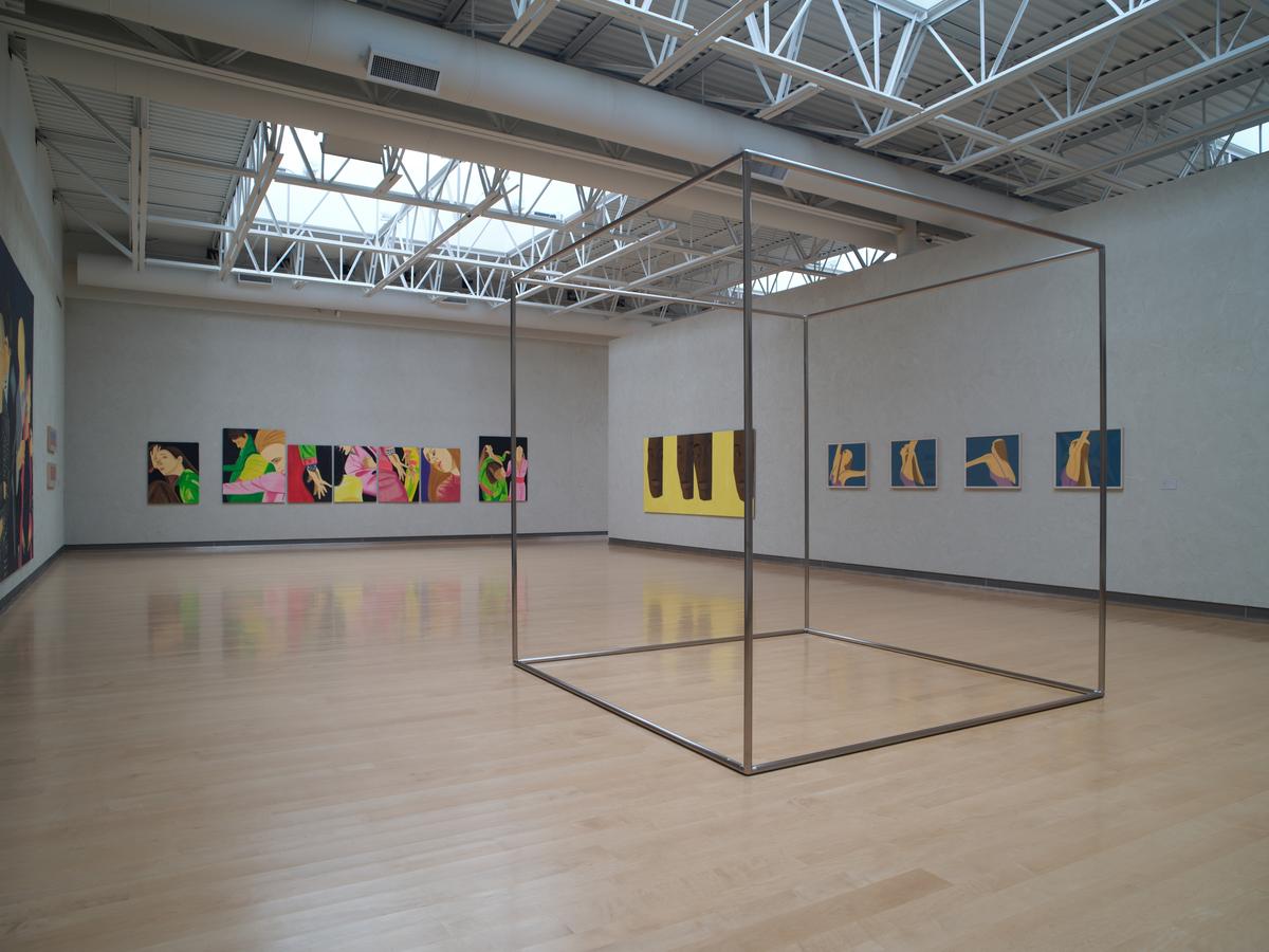 Gallery with geometric sculpture of an outlined cube surrounded by walls with colorful figurative paintings.