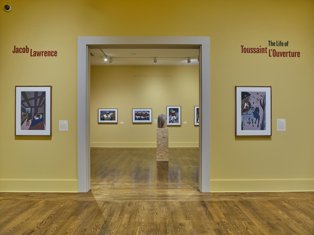 View through a doorway into a gallery featuring framed works with a stone sculpture at the center