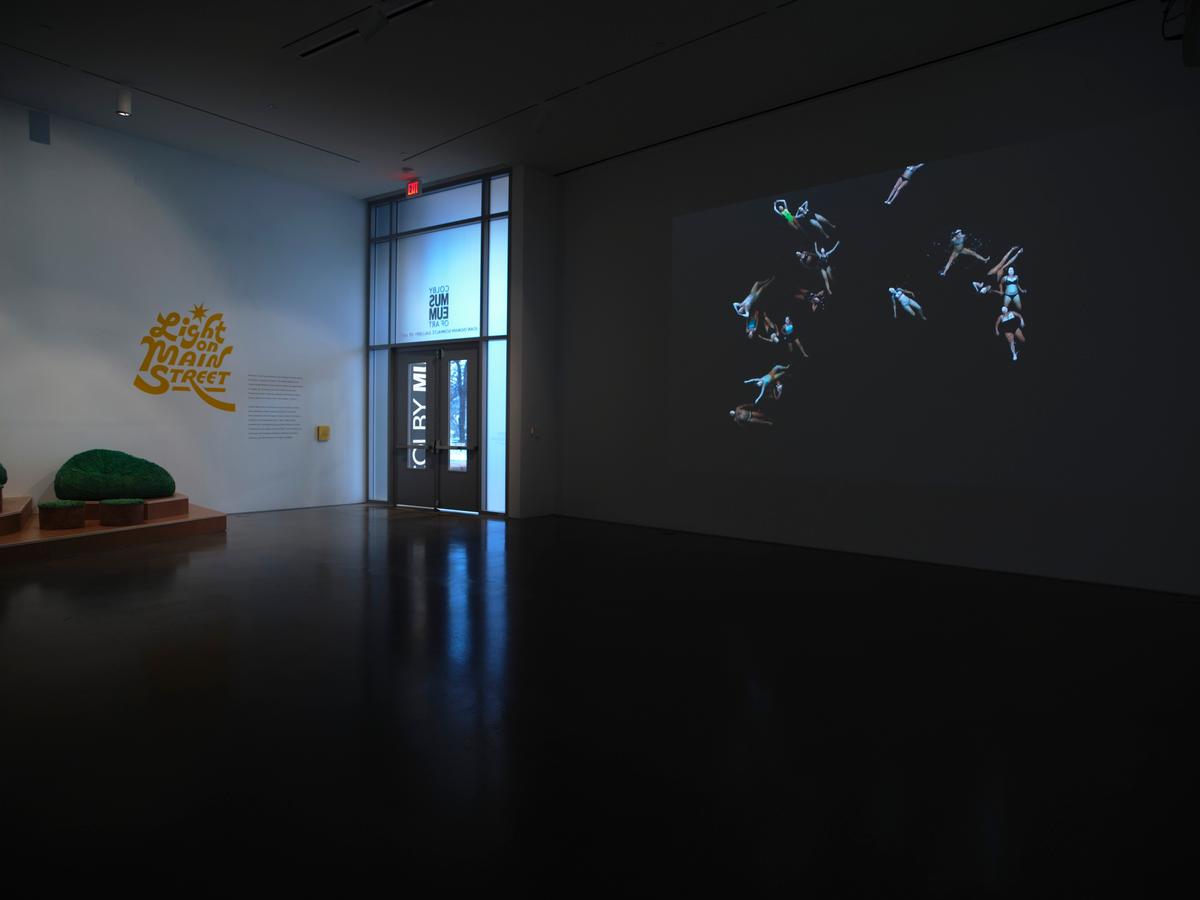 Dark gallery space with projected video of floating figures.