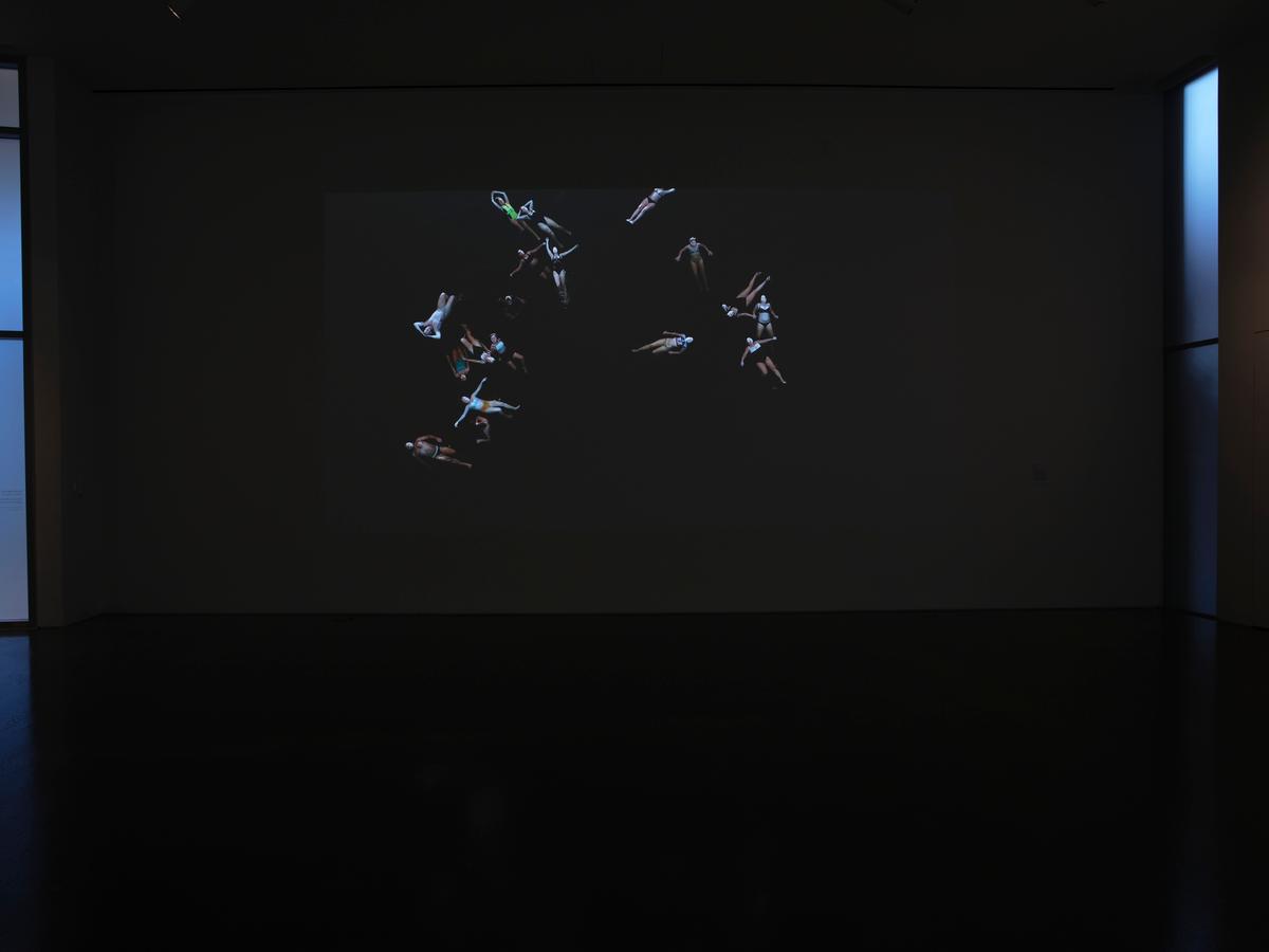 Projected video of floating figures on a dark gallery wall.