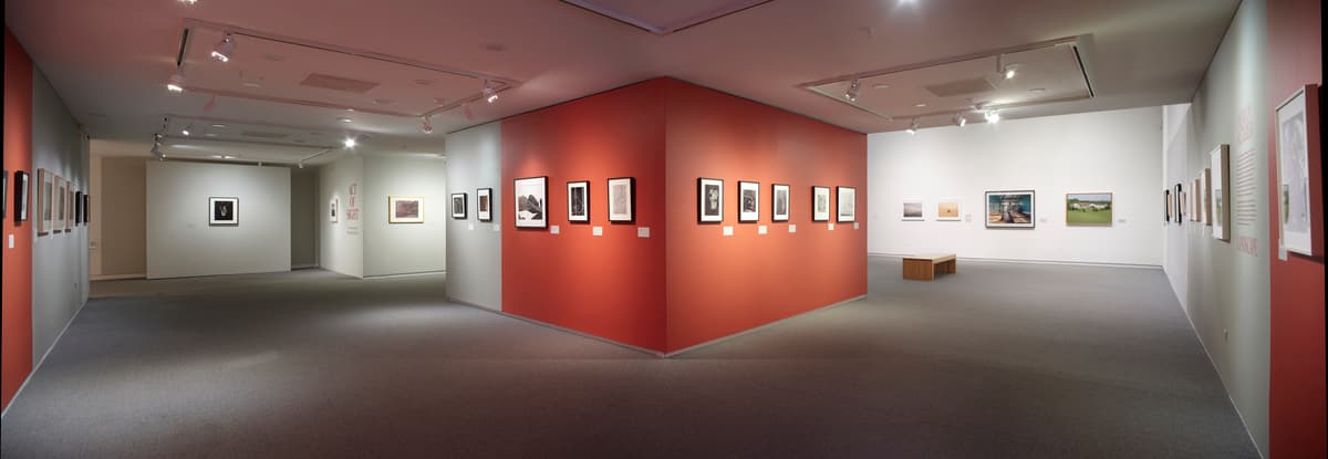 Panoramic view of gallery with red and white walls displaying framed photographs in multiple rooms