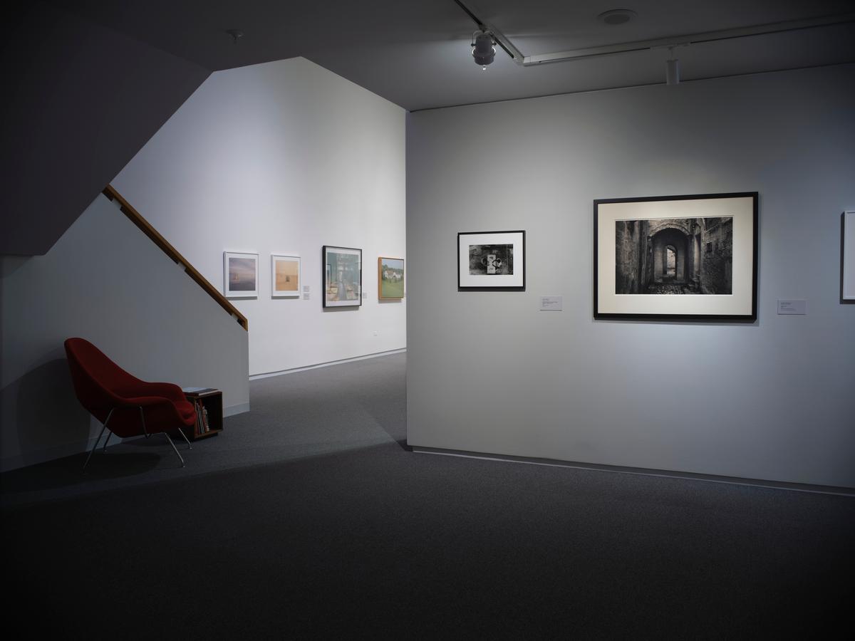 Framed photographs on gallery walls with a red chair near a staircase