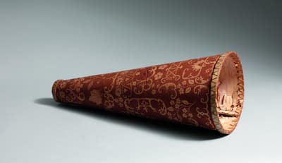 Cone-shaped object made of reddish patterned material resting on a light surface