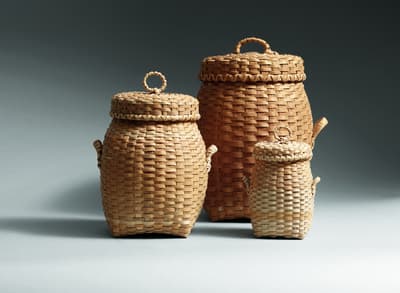 Three lidded woven baskets of different sizes arranged on a light background