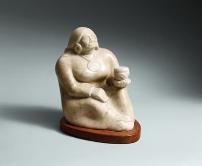 Sculpted seated figure holding a small basket on a wooden base, set against a light background
