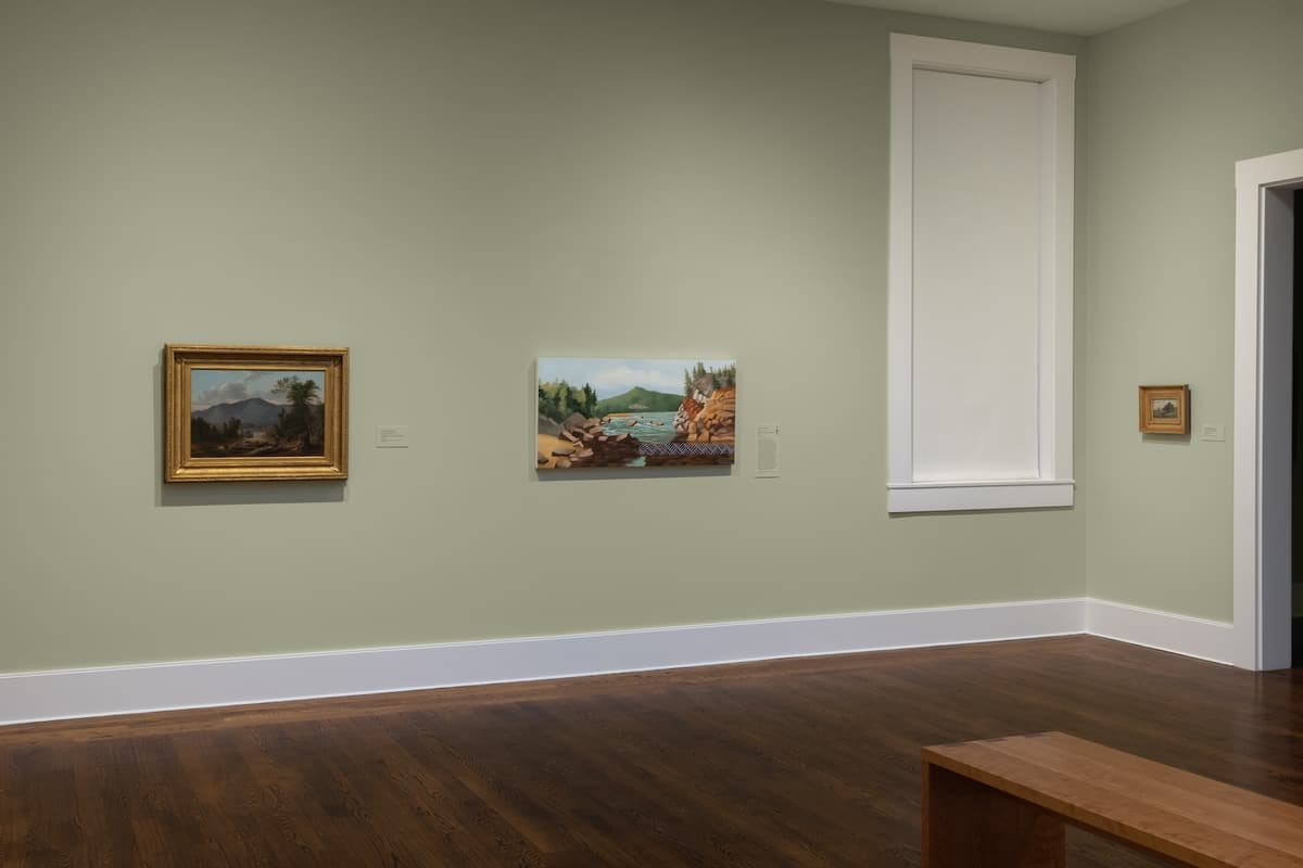 Three framed landscape paintings on a pale green wall, one including a panoramic scene