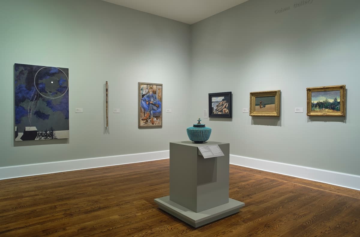 Contemporary basket on pedestal with five diverse artworks on surrounding green walls.
