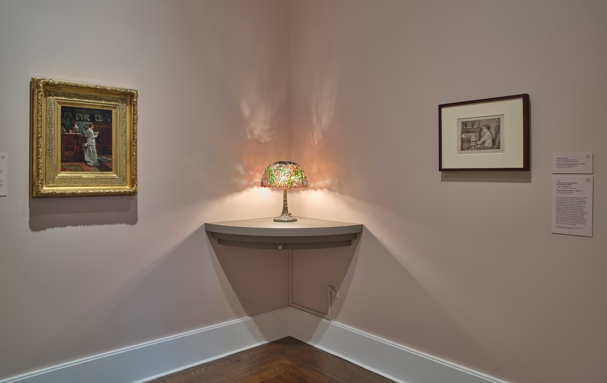Corner display with a Tiffany lamp and two framed artworks on pink walls.